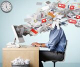 Overwhelmed business owner buried under emails and paperwork at desk, illustrating need for virtual assistant services for inbox management, delegation, and business automation.